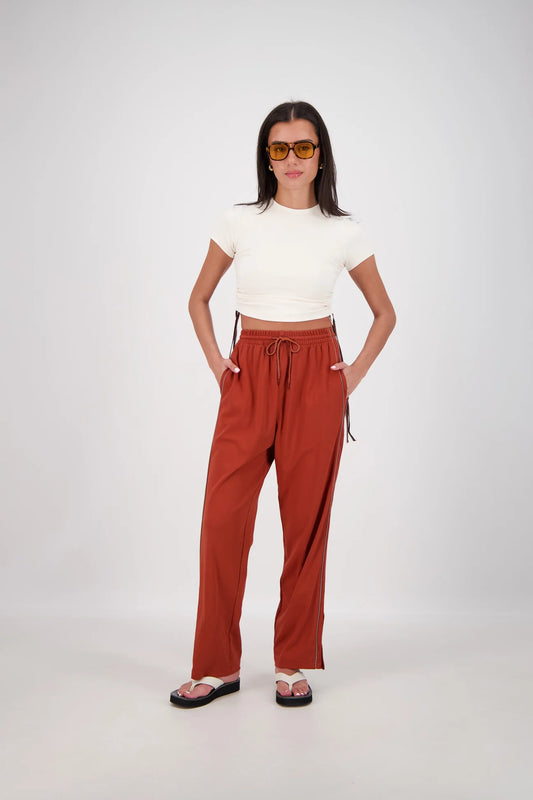 Woman wearing a white top and rust-colored pants on a white background